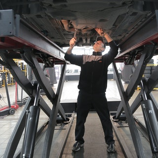 mechanic standing under raised car fixing it from underneath