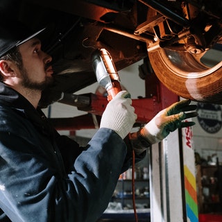 mechanic under a car inspecting break lines and tyres